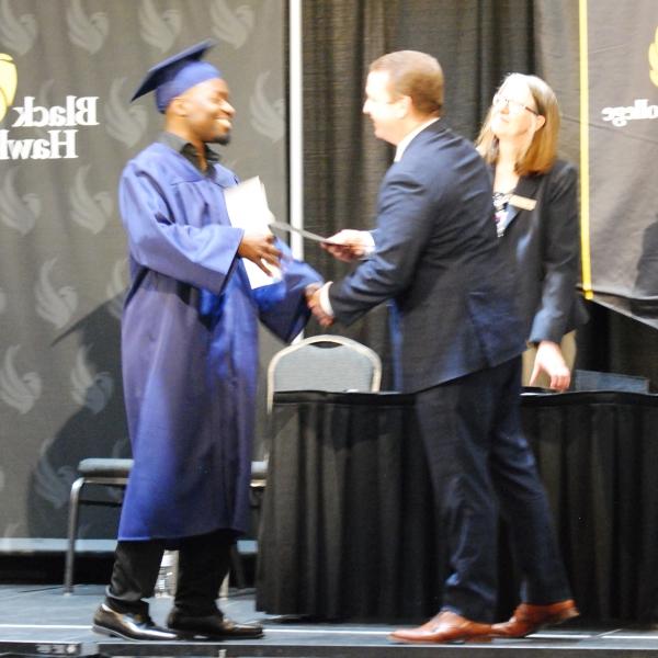 BHC总裁博士. 杰里米·托马斯在台上向普通教育文凭毕业生托尼·约翰逊颁发证书